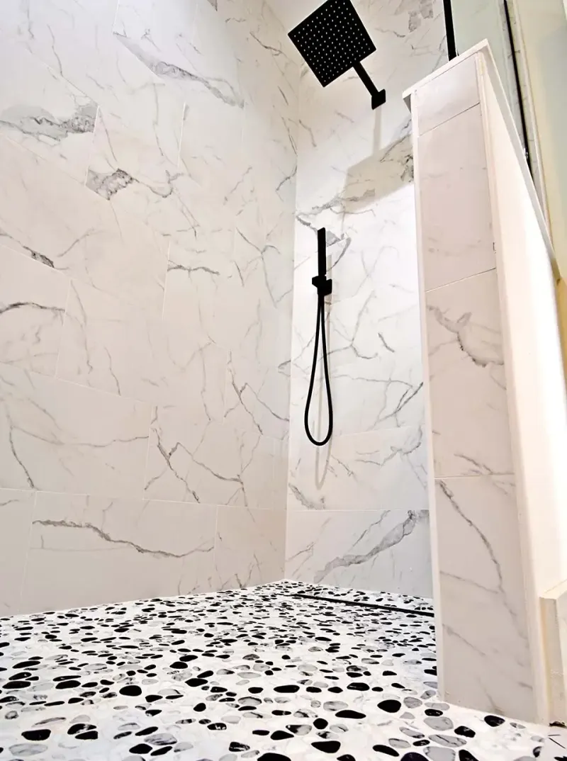 Shower with white marble-look walls, black-and-white pebble mosaic floor and matte black fixtures