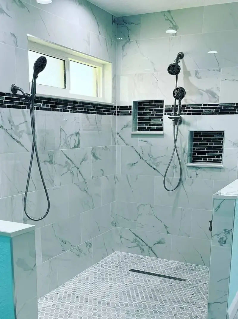 Walk-in shower with marble-look wall tile, black accent band and recessed niches